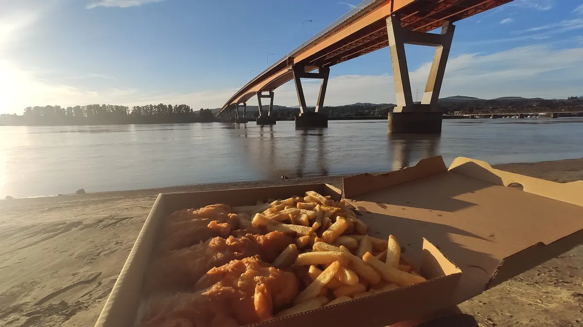 Fish and chips in a box by a river with a bridge